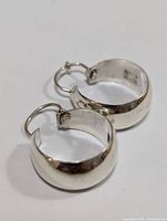 Pair of silver hoop earrings on white background, viewed from an angle showing the outer smooth surface and hinges.