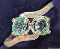 Close-up of silver emerald ring showing two green oval emerald stones with prong settings.