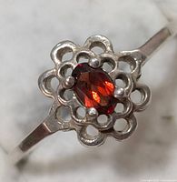 Close-up photo of silver ring with oval garnet gemstone and floral silver setting.