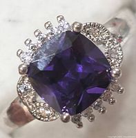 Close-up front view of silver ring with a large cushion-cut purple gemstone surrounded by clear stones.