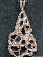Close-up of the silver pendant showing its organic, irregular openwork design and textured surface.