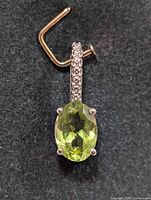 Front view of silver pendant with oval-cut green peridot and cubic zirconia stones on the bail.