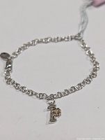 Silver rhodium plated bracelet with 'T' pendant and small diamond accent, shown laid flat.