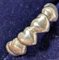 Close-up image of the silver ring showing the heart-shaped elements on a soft blue background.