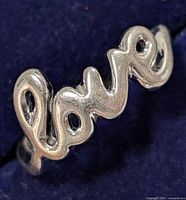 Close-up of silver ring spelling out 'love' on a dark blue background showing the cursive script design and shiny silver finish.