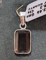 Close-up front view of rectangular faceted smokey quartz gemstone pendant set in silver with attached price tag