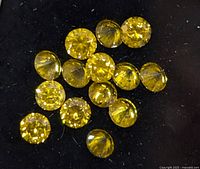 Close-up image showing multiple small, round yellow lab-grown diamonds with faceted cuts on a black background.