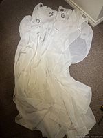 Six white sheer curtains laid out on carpet showing metal grommets at top edge and fabric texture.