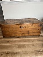 Front view of antique wooden chest showing metal handle, stained wood with visible scratches and wear