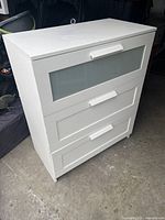 Front view of white BRIMNES IKEA 3-drawer dresser showing frosted glass on top drawer and white handles.