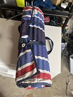 Rolled and strapped colorful striped beach mat, showing red, purple, blue, and white horizontal stripes.