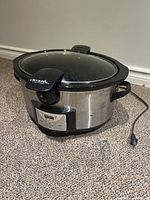 Side view of the Crock-Pot slow cooker showing stainless steel body, black plastic handles, glass lid, and control panel.