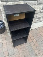 Full view of the dark wood bookshelf showing three shelves and peg holes for adjustability. Moderate wear on edges and surfaces visible.
