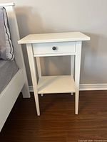 Front view of white IKEA HEMNES nightstand next to bed, showing drawer and shelf.