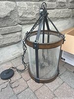 Full view of the industrial ceiling hanging light fixture showing dark bronze metal frame, wood accents at top and bottom, and clear textured glass panels. Hanging chain and ceiling mount plate visible.