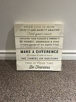 Photo of square wooden inspirational wall art plaque showing front face with multiple quotes in different fonts in black text on natural wood.