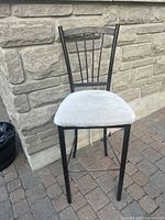 Front view of the black metal stool with grey cushioned seat and solid backrest.