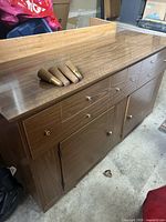 Front and top view of wood veneer sideboard showing drawers, cupboards, and removed legs resting on top.