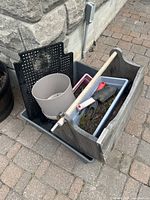 Wooden gardening tool organizer filled with gardening hand tools, and several plastic planters of different sizes and colors, placed on paved outdoor ground.