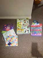 Photo showing all 6 multicolor party gift bags arranged on floor including animal theme, stripes, polka dots, and cake designs