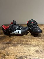 Pair of Peloton black and red women's cycling shoes placed on wooden surface, showing side and top views of left and right shoes.