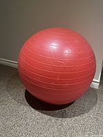 Red workout ball sitting on carpeted floor, showing side view with horizontal texture lines.