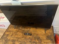 Front view of TV powered off on wooden table with remote below screen
