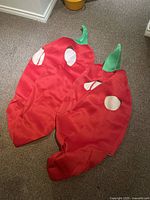 Two red chili pepper costumes on carpet showing front view with white spots and green fabric stems