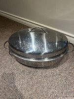 Closed view of oval stainless steel roasting pan with lid on top, showing side handles and lid handle.