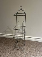 Front view of two-tier silver metal towel rack showing rectangular storage basket and top towel bar with twisted loop handle.