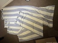 Four blue and white striped polyester curtains folded on the floor, showing metal grommets at the top edge.