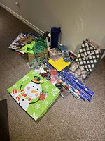 Overview of various Christmas-themed gift bags, tissue paper, and some wrapping paper rolls against a wall corner