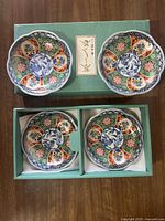 Lot of four multi-color floral porcelain plates shown on green box, two plates on top of box and two plates inside box compartments