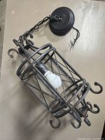 Full view of the vintage style hanging light fixture showing the dark grey metal cage frame with curled decorative elements and the bulb inside