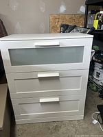 Full front view of the white three-drawer dresser showing the frosted glass top drawer and two solid front drawers.