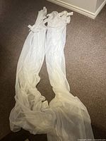 Two long white curtain panels laid on carpeted floor, showing length and fabric texture.