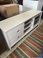 Wide angle shot of the white wood media console showing the two drawers, open shelves, and glass door.