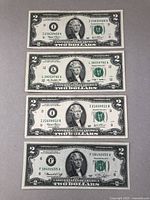 Four $2 bank notes laid out showing front side with portraits of Thomas Jefferson, serial numbers, and green treasury seals.
