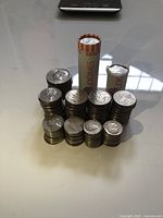 Full lot of American coins showing multiple stacks of half dollars, quarters, dimes, nickels, and pennies with two rolls of coins standing vertically