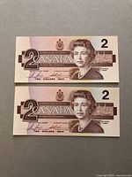 Two 1986 Canadian $2 bank notes stacked to show front design with Queen Elizabeth II portrait and denomination 2.