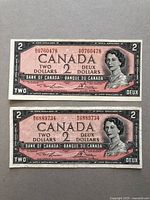 Two Canadian two dollar 1954 Series bank notes with visible serial numbers and portrait of Queen Elizabeth II.