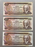 Three 1979 series $100 Canadian banknotes front sides laid out flat, showing portrait of Sir Robert Borden and serial numbers