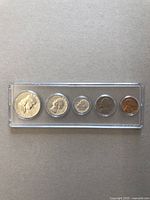 Five vintage American coins arranged side by side in a clear protective rectangular case, showing varying sizes and copper to silver colors.
