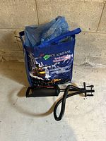 Photo of the blue carrying bag with Air Force design and attached manual pump hose and nozzle on concrete floor.