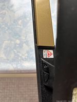 Close-up of the black and gold ceramic hair straightener showing temperature adjustment buttons and warning label.