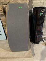 Top view of the wooden balance board showing gray grip tape surface for traction, placed standing against a stone wall.