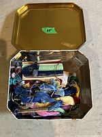 Top-down view of gold-tone metal craft box lid open showing embroidery floss and craft supplies inside.