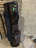 Black MacGregor golf bag standing against a wall, showing front and side compartments and carrying strap.