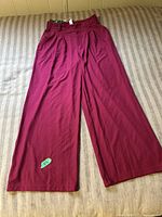 Front full view of burgundy wide leg pants with tags, laid flat on a bed.