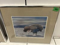 Framed Inuit art print showing a person in a brown parka bending over on snow with a winter landscape background.